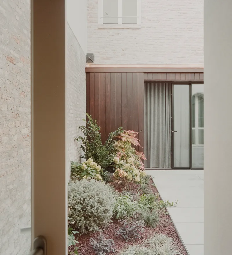 Narrow courtyard passage framed by painted brick walls with low plantings along the paved floor