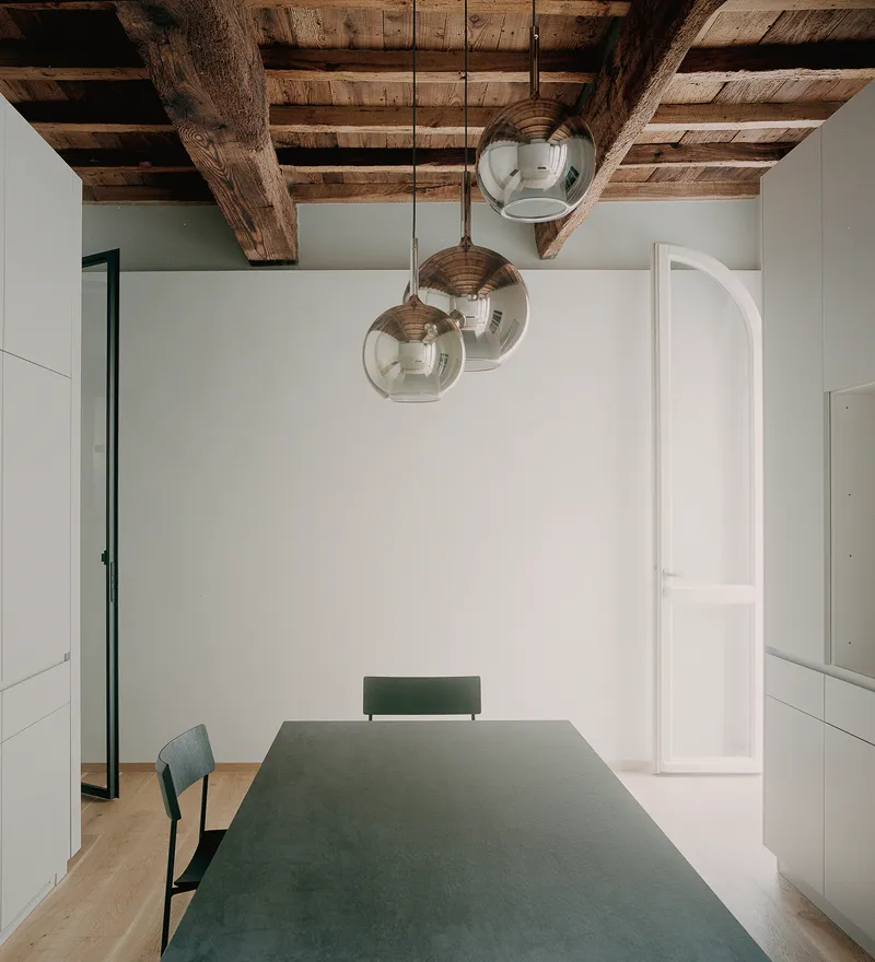 Dining area with green table under three glass pendant lights and exposed timber ceiling beams