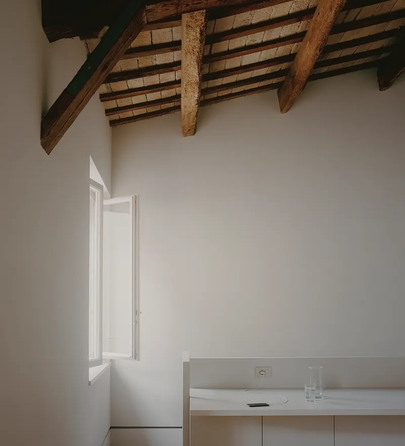 Interior corner with exposed timber beam ceiling and a tall window casting soft afternoon light
