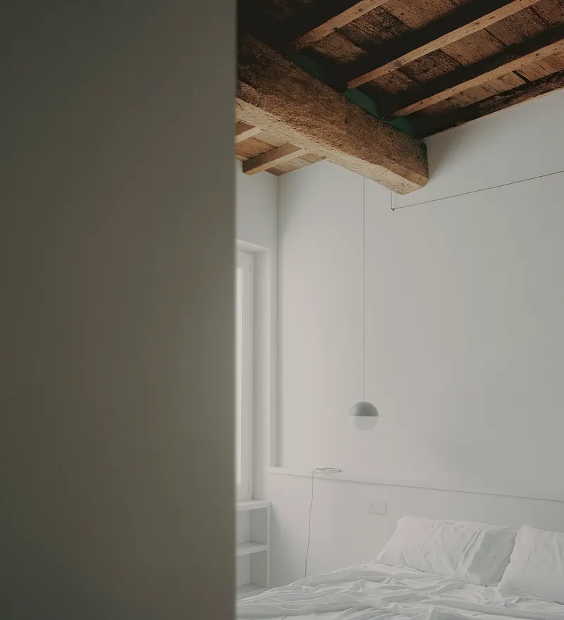 Bedroom view through a doorway showing a pendant light and exposed ceiling beams in soft daylight