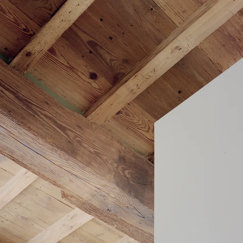 Detail of exposed timber beams and reclaimed wood planks meeting a white painted wall
