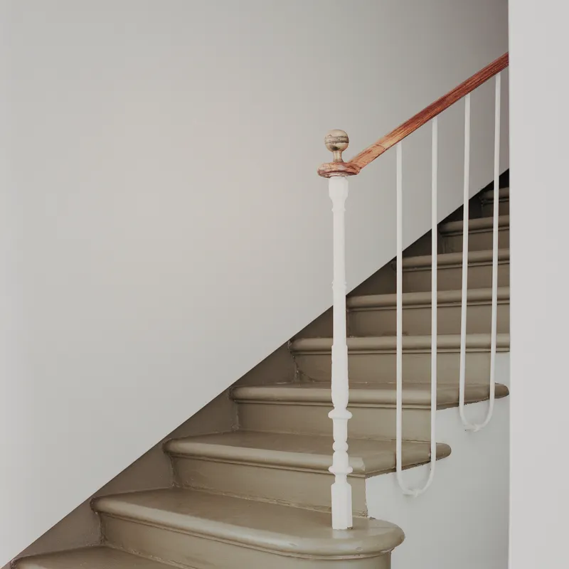 Curved staircase with turned white newel post and minimal steel rod railing ascending upward