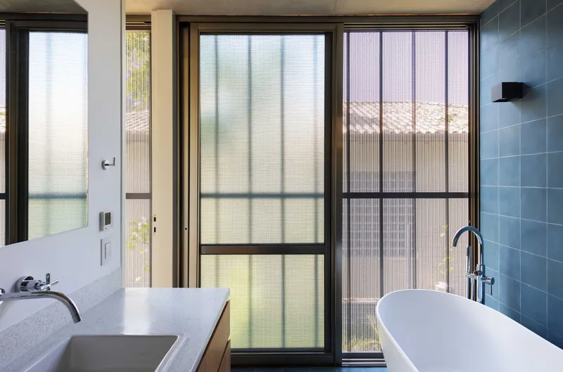 Bathroom with freestanding tub and translucent glass doors overlooking courtyard beyond
