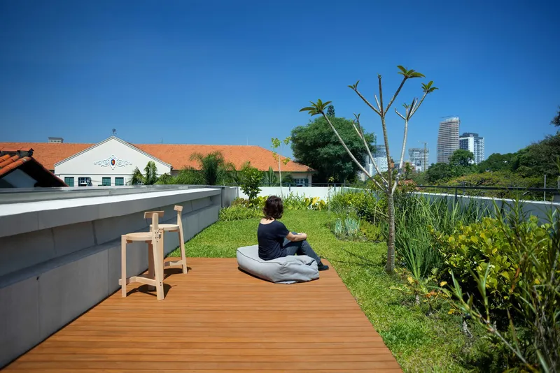 Rooftop garden terrace with timber deck and person sitting among planted beds under clear sky