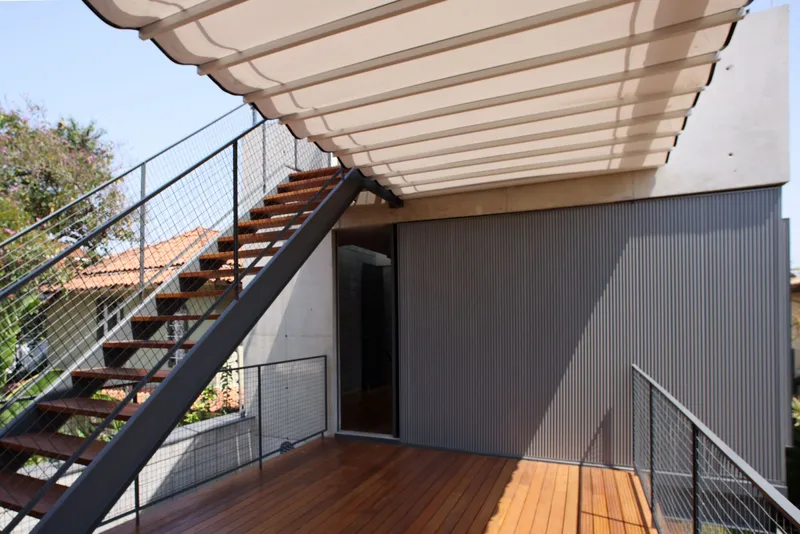 View of the slatted timber canopy overhead and corrugated metal wall beside the wooden deck