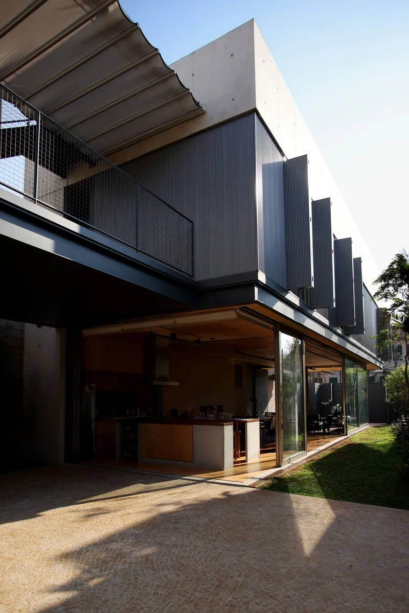 Open kitchen pavilion with timber ceiling extending toward a lawn in afternoon shadow