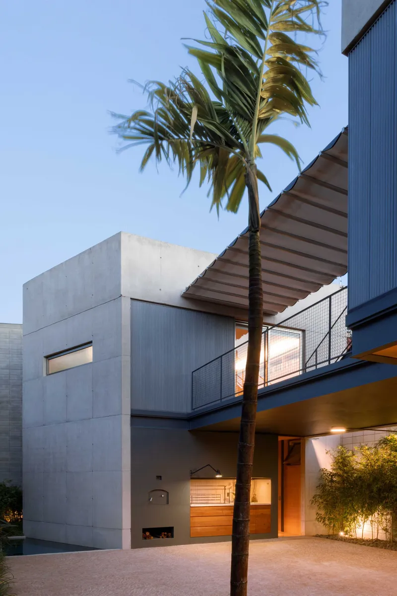 Concrete volumes with horizontal window openings and a palm tree at dusk with interior lights on