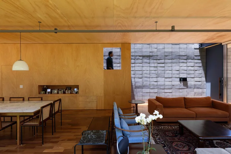 Open living space with plywood ceiling and walls, white tiled accent wall, and person passing through doorway