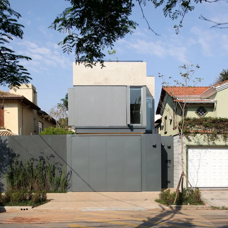 Street facade with stacked grey volumes and white concrete upper level framed by neighboring tile-roofed houses