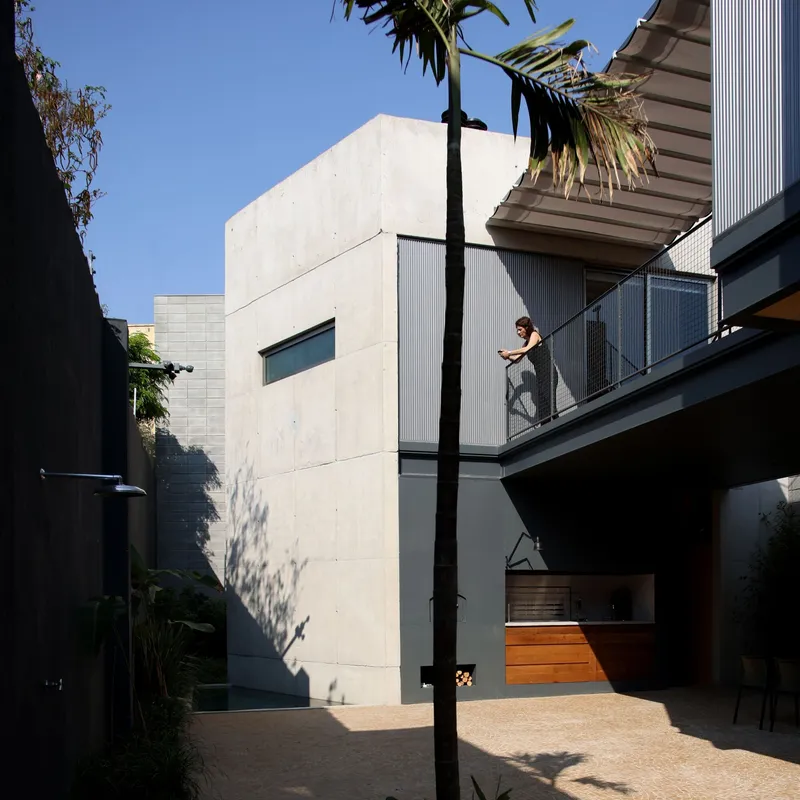 Courtyard view showing concrete volume, corrugated metal balcony, and person standing on upper terrace