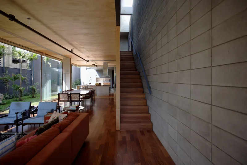 Interior staircase ascending along gridded concrete block wall with plywood ceiling and garden view