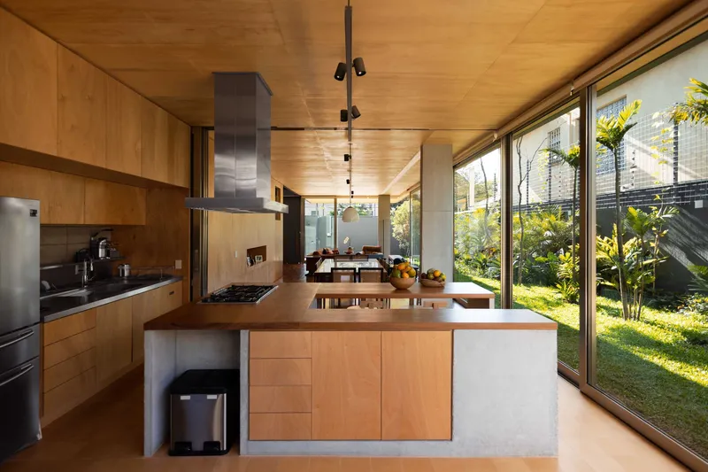 Open kitchen with timber island and concrete details overlooking planted garden through full-height glazing