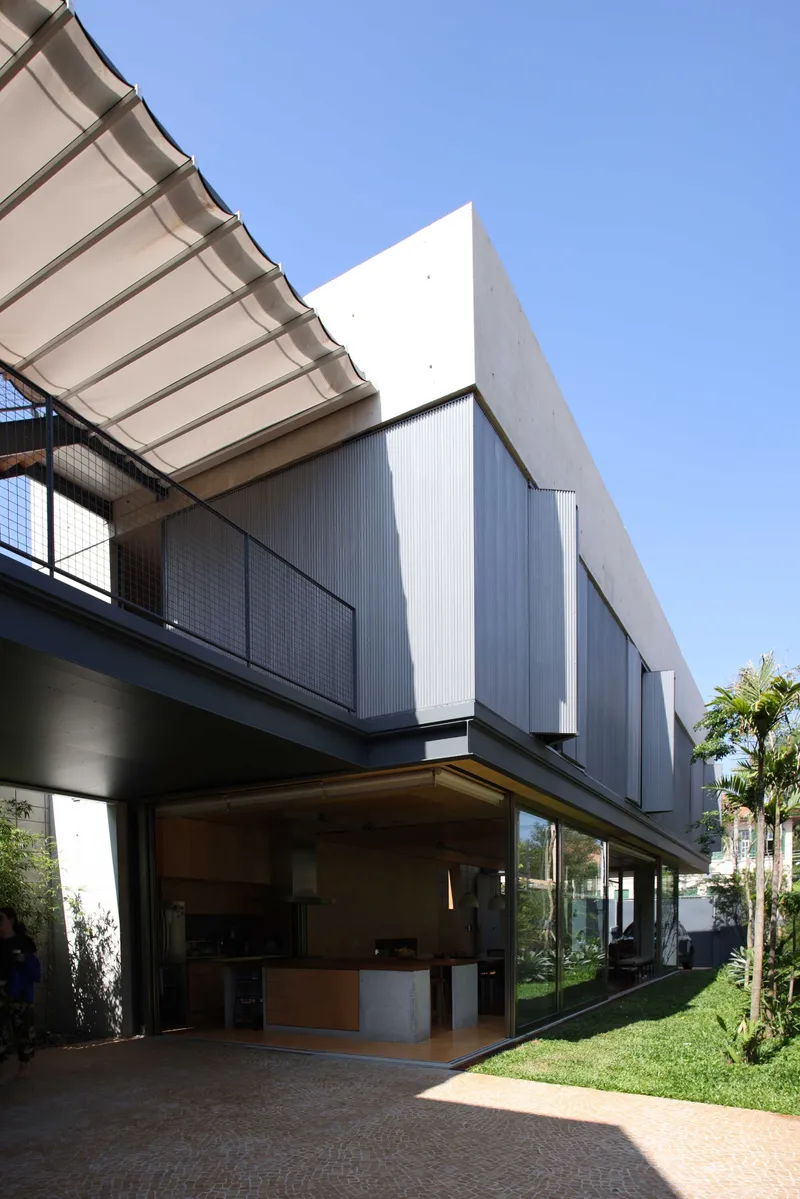 Cantilevered upper volume with corrugated metal cladding and retractable awning over open ground floor