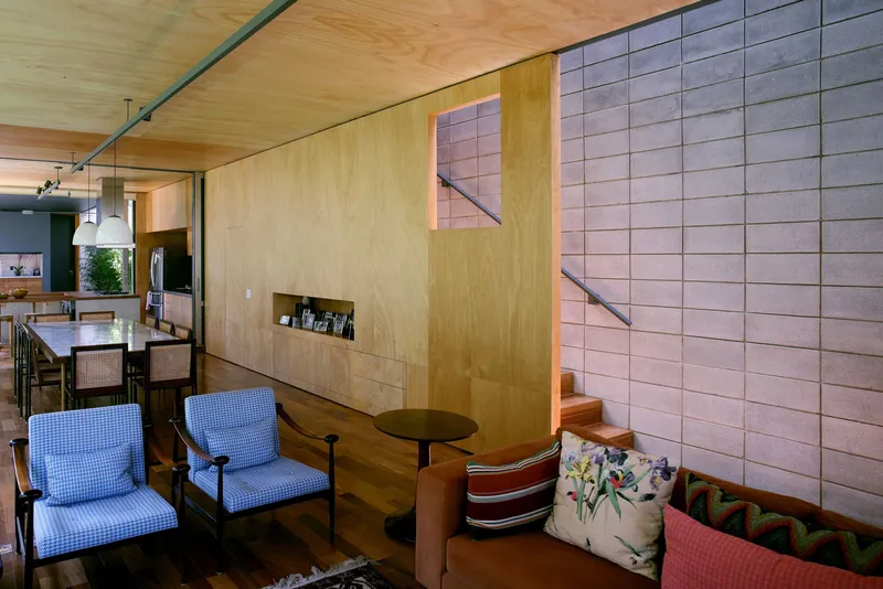 Living room with plywood-clad walls and pink tile wall illuminated by afternoon sunlight
