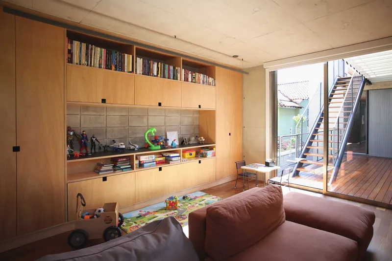 Living room with built-in plywood shelving and open doors framing a timber deck and exterior stair