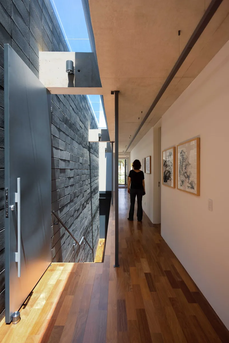 Upper hallway with figure standing before framed artworks and textured tile wall opening to sky
