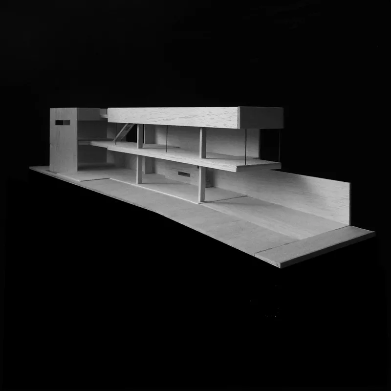 Physical model showing horizontal planes and recessed volumes on a sloped site against black backdrop