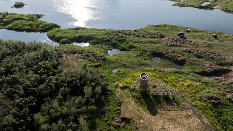 Top-down view of the concrete cylinder and timber grid platform casting shadows across the grassy wetland terrain