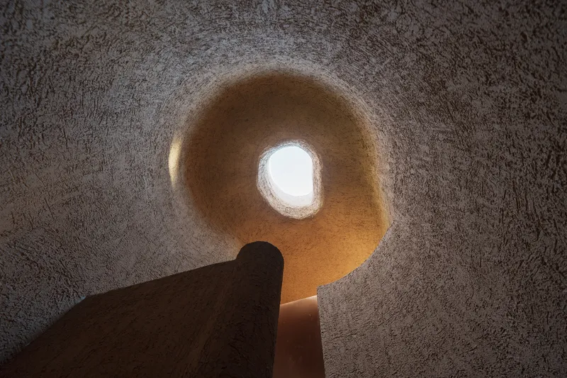 Upward view through a circular skylight opening in a textured earthen dome with a single pendant light