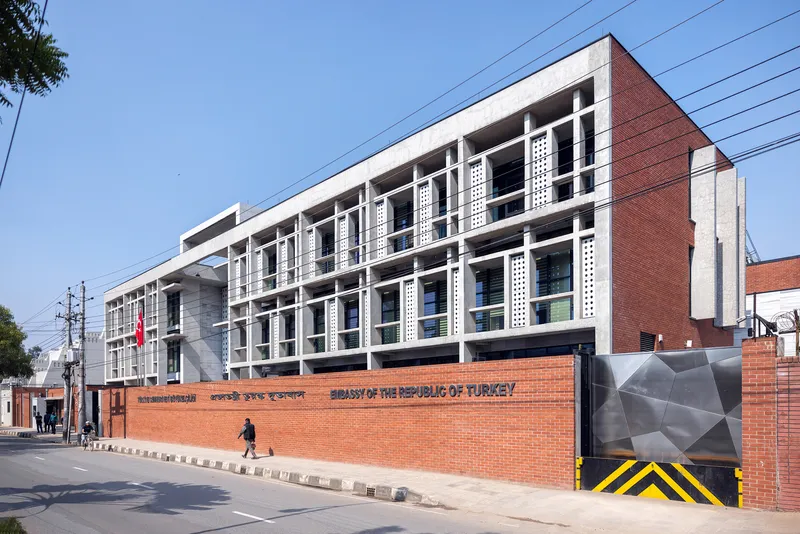 Oblique view showing the white concrete grid facade rising above the red brick perimeter wall