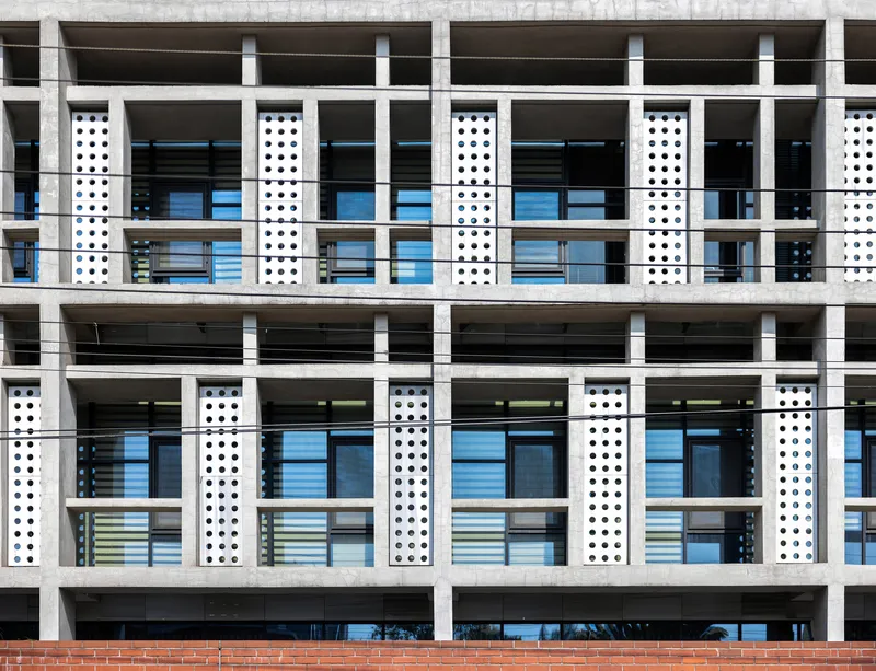 Close-up of the white concrete frame facade showing perforated vertical panels and horizontal floor slabs