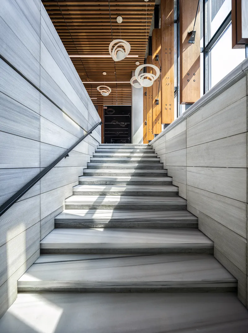 Interior staircase with ribbed wall panels and timber slatted ceiling lit by circular pendant fixtures