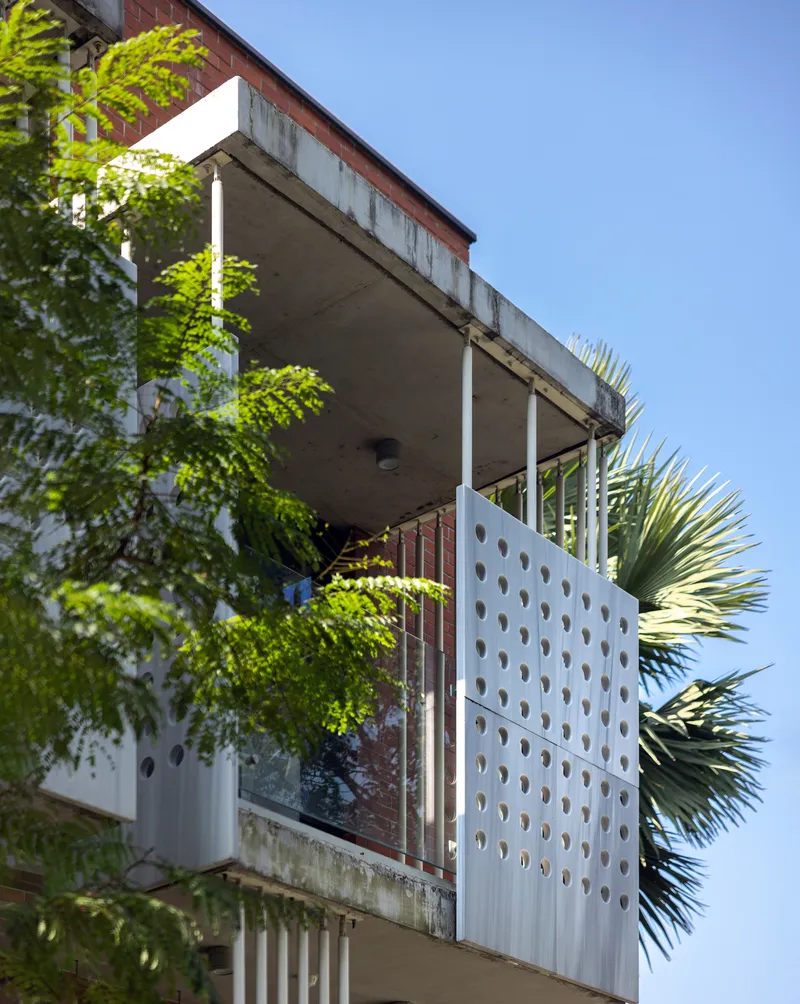 Corner balcony with perforated metal screen and planted greenery against a clear blue sky