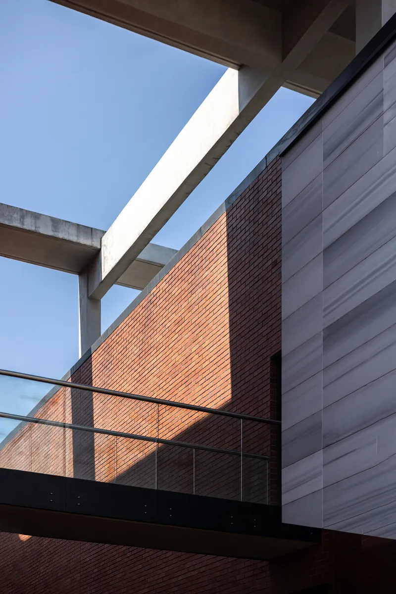Upward view of the red brick wall intersecting concrete frame and glass balcony railing