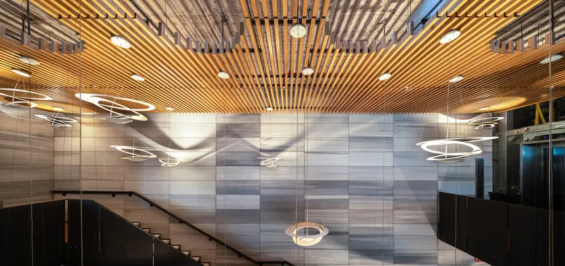 Interior lobby with slatted timber ceiling and circular pendant lights above the striped stone wall