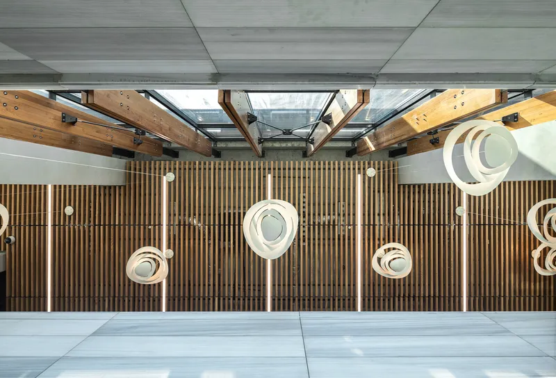 Top-down view of a timber-slatted wall with suspended circular pendant lights and exposed steel roof trusses
