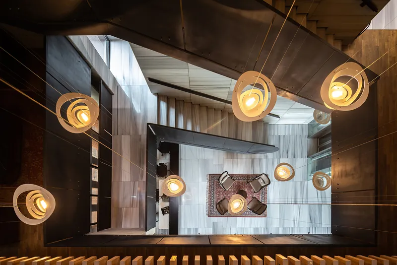 Looking down the stairwell with tiered pendant lights illuminating mixed material walls and tiled floors