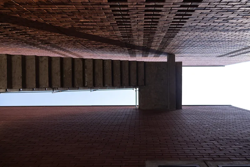 Covered brick courtyard with patterned timber ceiling and concrete columns framing the open plaza
