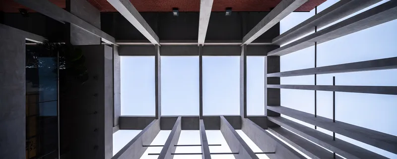 Upward view through an atrium with horizontal concrete fins and glazing open to pale sky