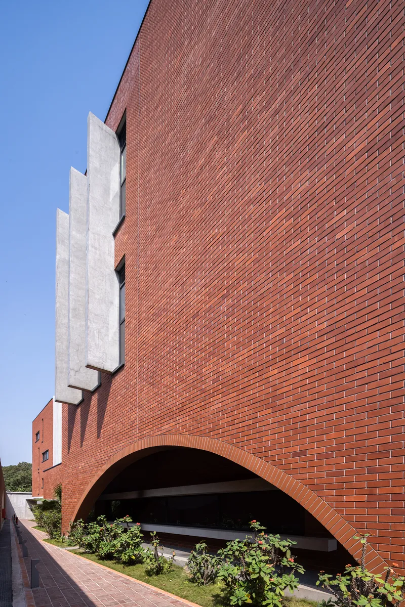 Diagonal brick facade with recessed concrete stairwell and arched opening above landscaped planter beds
