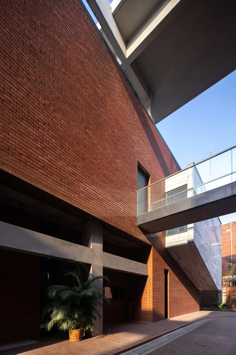 Courtyard entry framed by red brick walls, concrete bridge overhead, and a palm tree in shadow