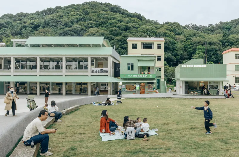 Terraced lawn in front of pale green buildings with people picnicking and walking under overcast skies