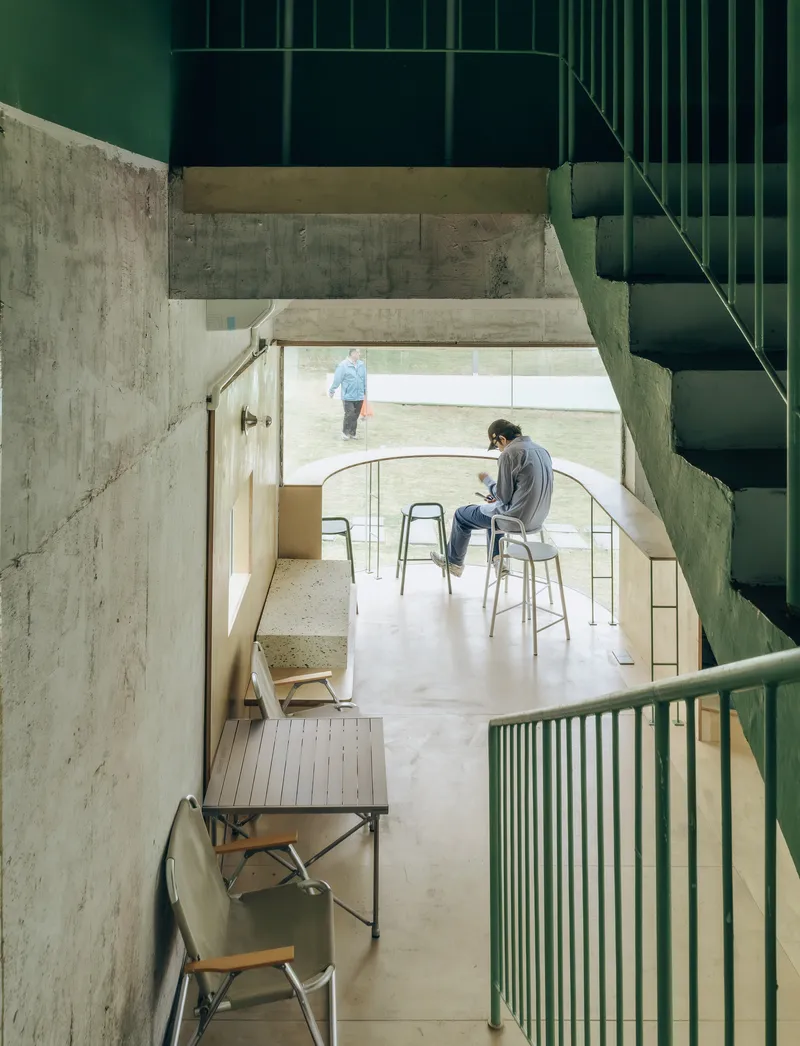 Split-level interior showing concrete walls, green metal staircase, and terrazzo flooring with seated occupants