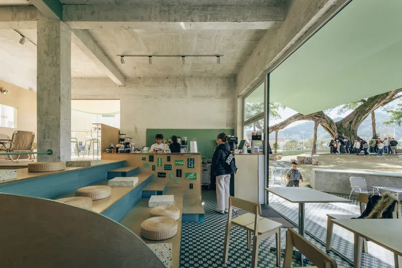 Cafe counter with stepped blue bench seating and large window framing a gnarled tree outside