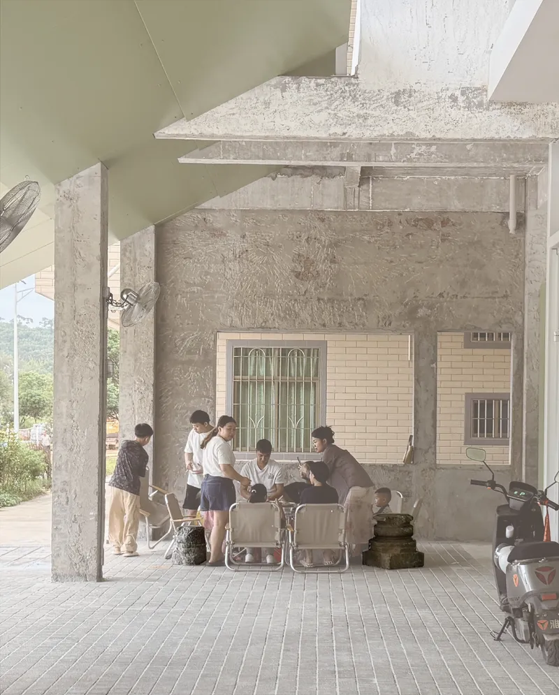 Covered outdoor porch with concrete columns where visitors gather around folding chairs in afternoon light