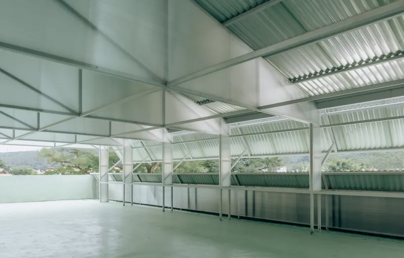 Covered rooftop terrace with corrugated metal ceiling, exposed steel trusses, and translucent green wall panels