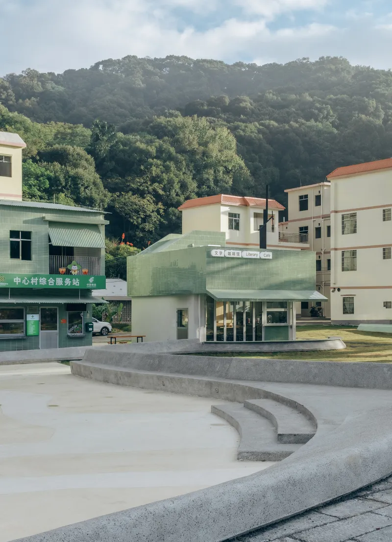Curving concrete terraces in a plaza facing a compact pale green library pavilion with tile-clad upper volume