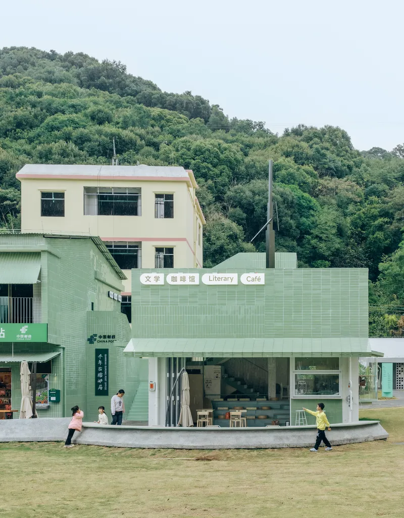 Single-storey library and cafe pavilion clad in pale green tiles with children running across the lawn