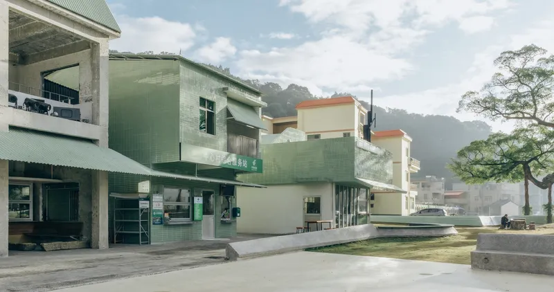 Public plaza with pale green corrugated metal buildings and concrete steps under partly cloudy skies