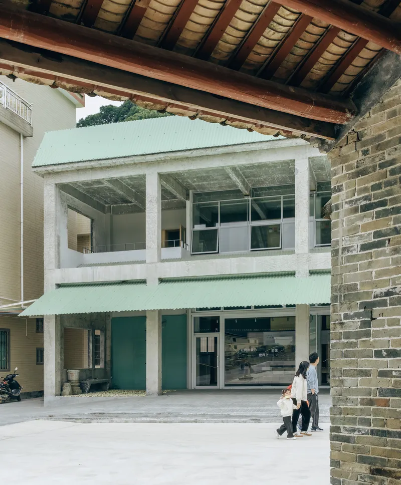 Covered arcade framing a pale green volume with white concrete columns as a family walks through
