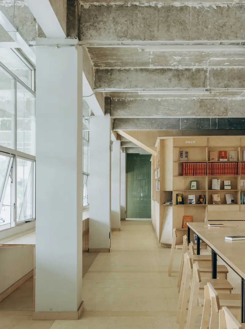 Interior library space with exposed concrete ceiling beams and light wood reading tables and bookshelves
