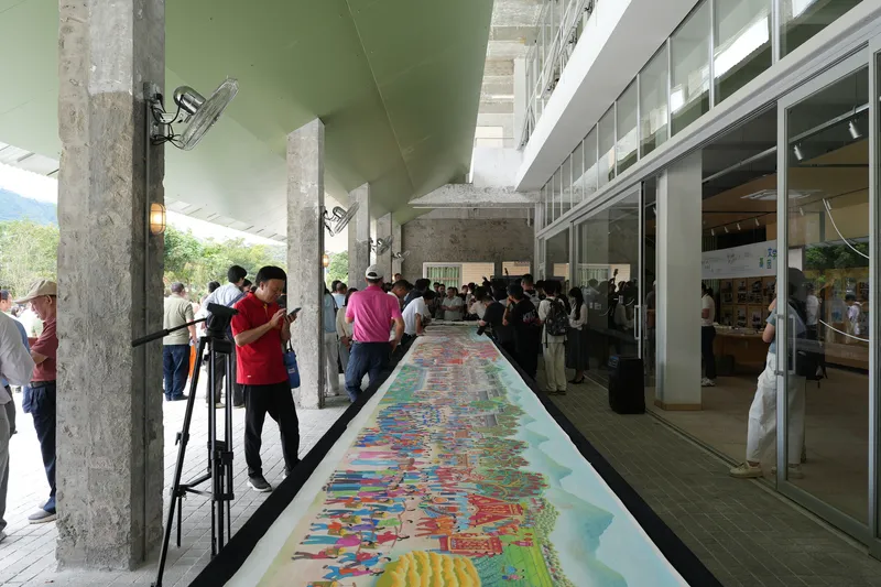 Covered exterior corridor with concrete columns and visitors viewing a long painted mural on the floor