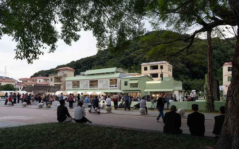 Evening view of the pavilion with open glass facade and crowd gathering on the plaza