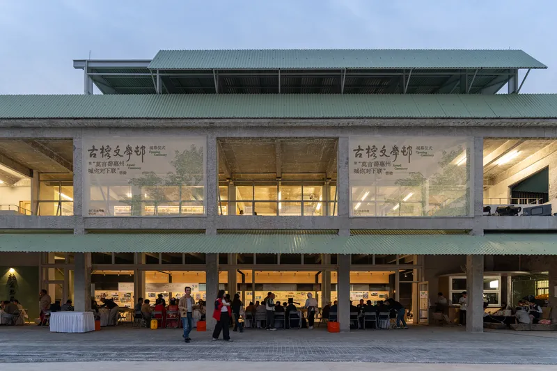 Two-storey facade with exposed timber beams, green corrugated roof and glazed infill panels at dusk