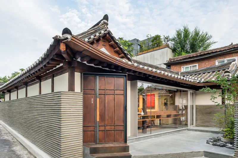 Exterior view of the renovated hanok with traditional tiled roof and ribbed metal facade under cloudy skies