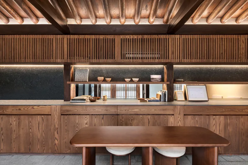 Kitchen workspace with timber counter, vertical slatted wall panels and exposed ceiling beams with indirect lighting